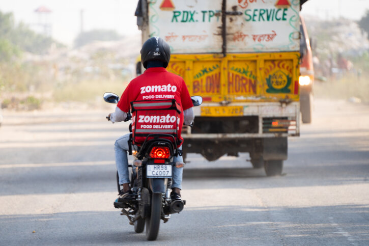 Delhi, India - circa 2022 : bike rider delivery boy with hot box branded with zomato the food tech delivery app in India and the iconic red uniform